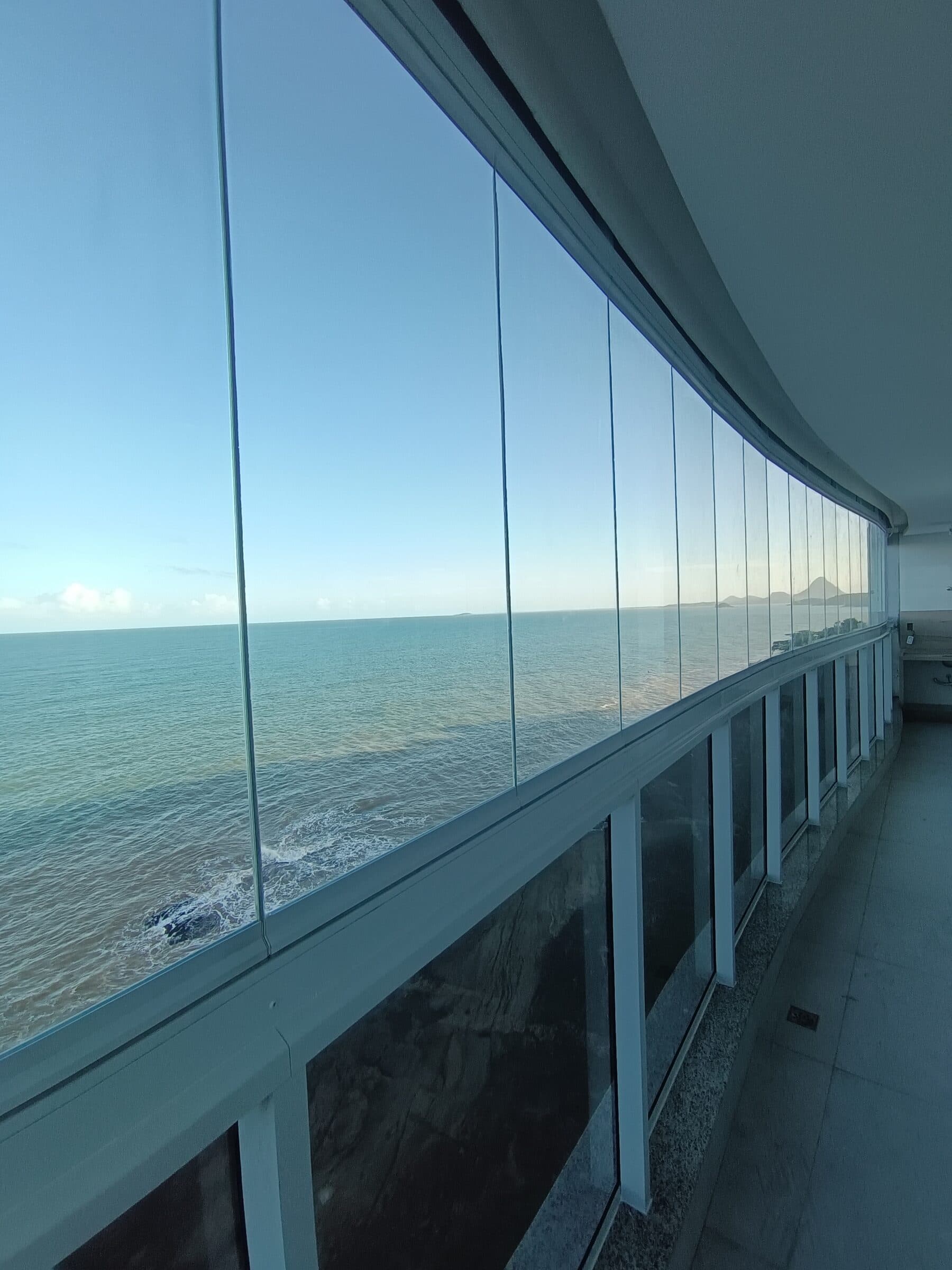 Vidros do fechamento de varanda alinhados, com vista para o mar aberto